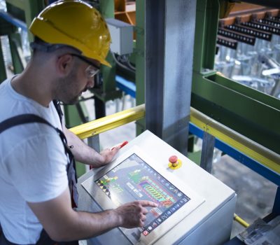 Factory worker monitoring industrial machines and production remotely in control room.