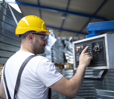 Factory worker operating industrial machine and setting parameters on the computer.